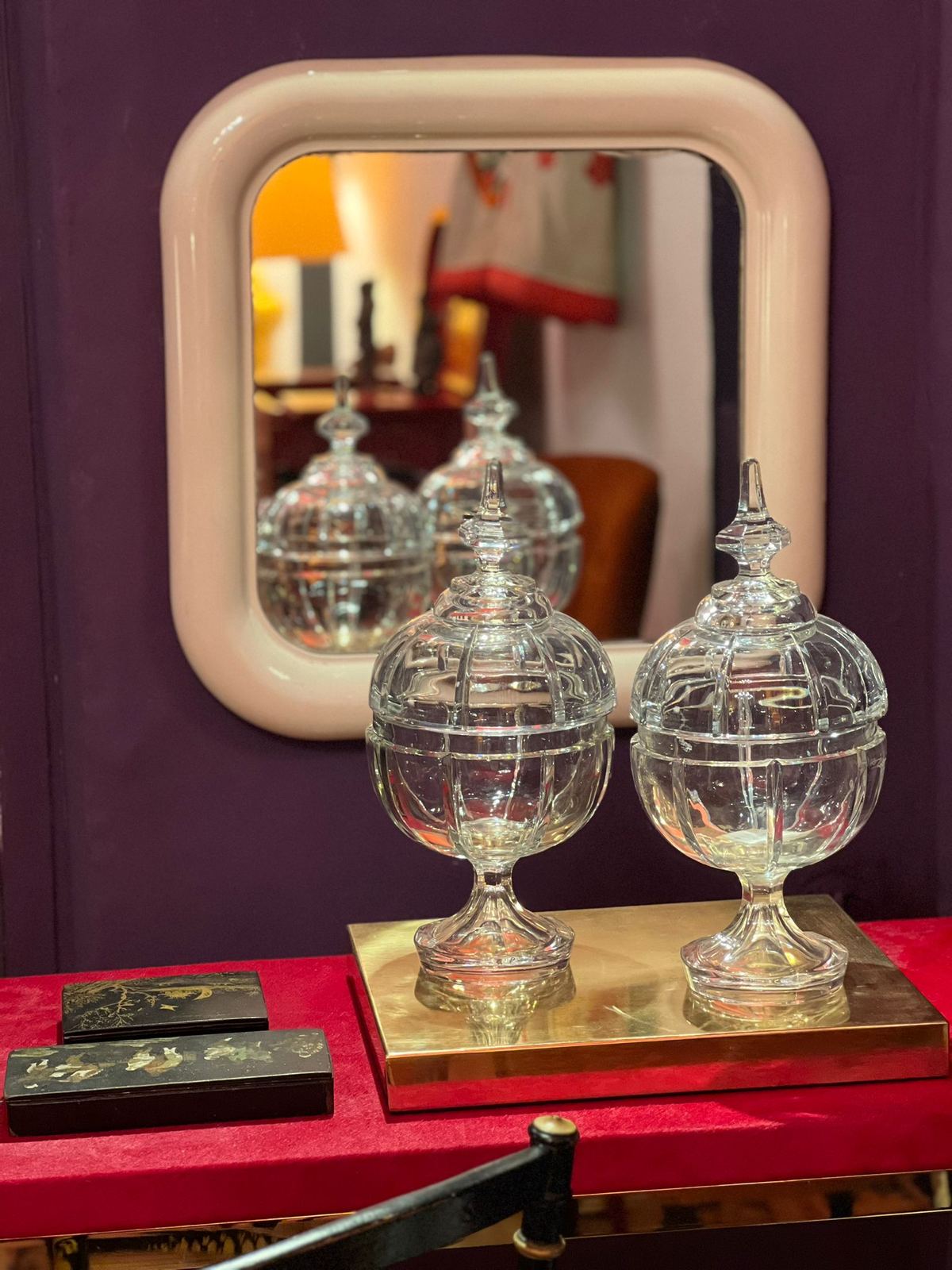 Two cut-crystal jars in front of a rounded mirror