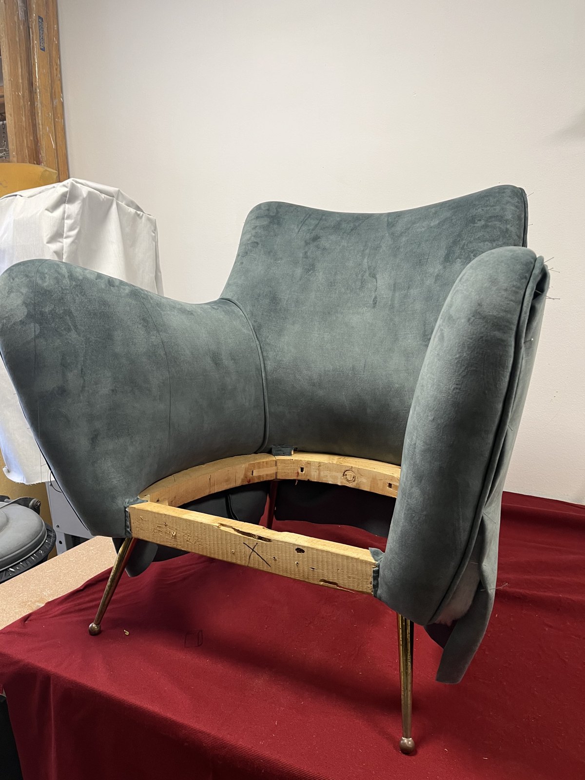 Armchair mid-restoration: new green velvet on the shell, bare wooden seat frame, brass legs