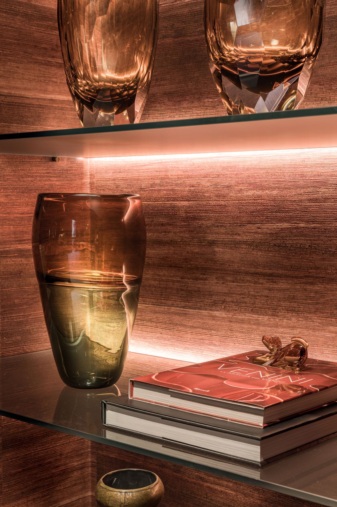 Amber glass vases and books on a lit glass shelf
