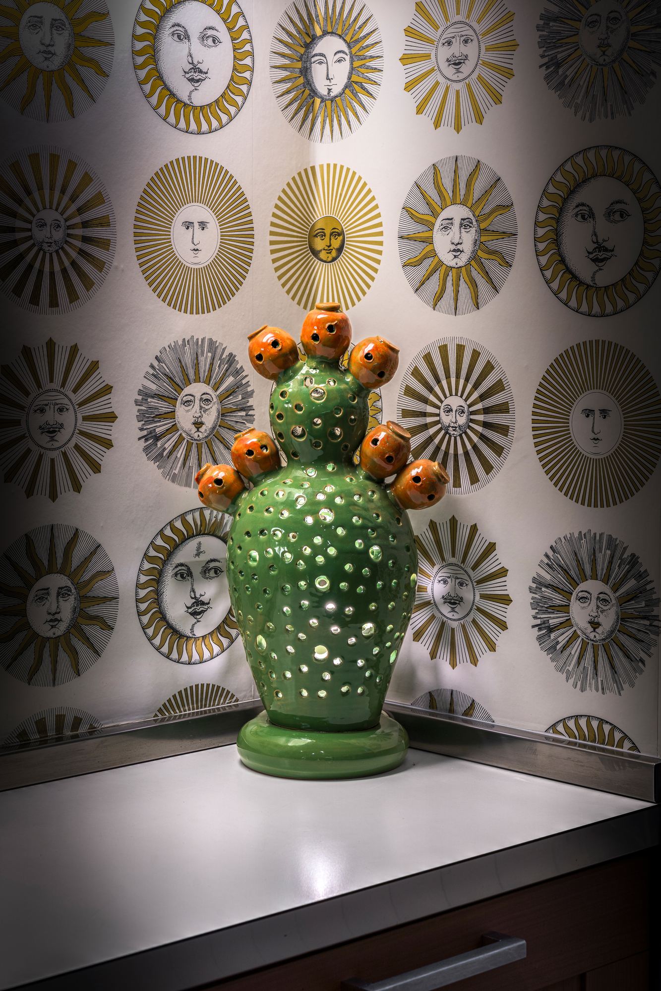 Green ceramic cactus against wallpaper patterned with suns