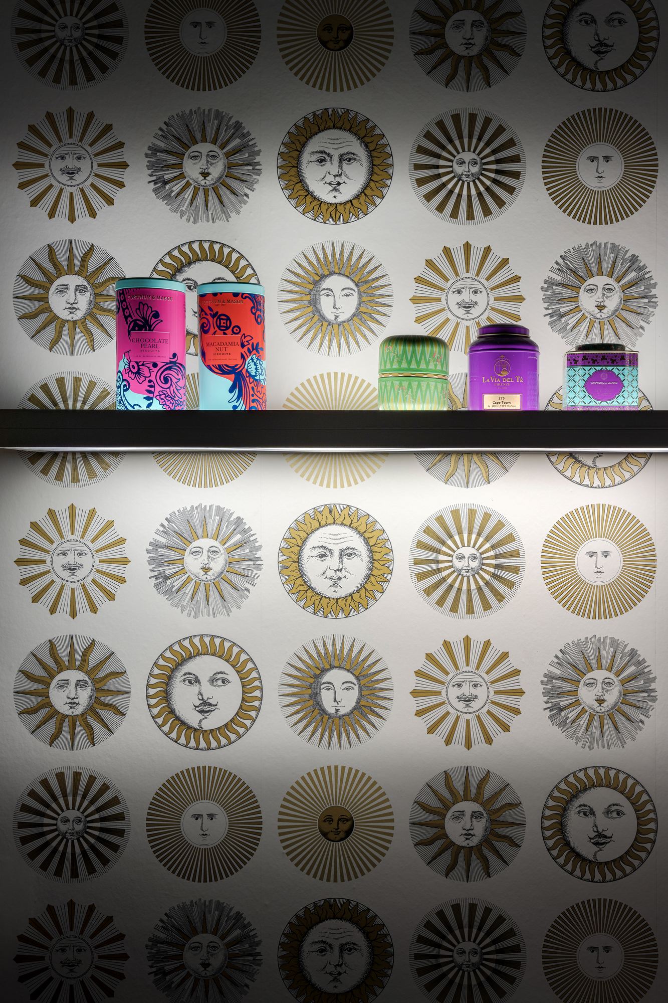 Coloured glass jars on a shelf against wallpaper patterned with suns