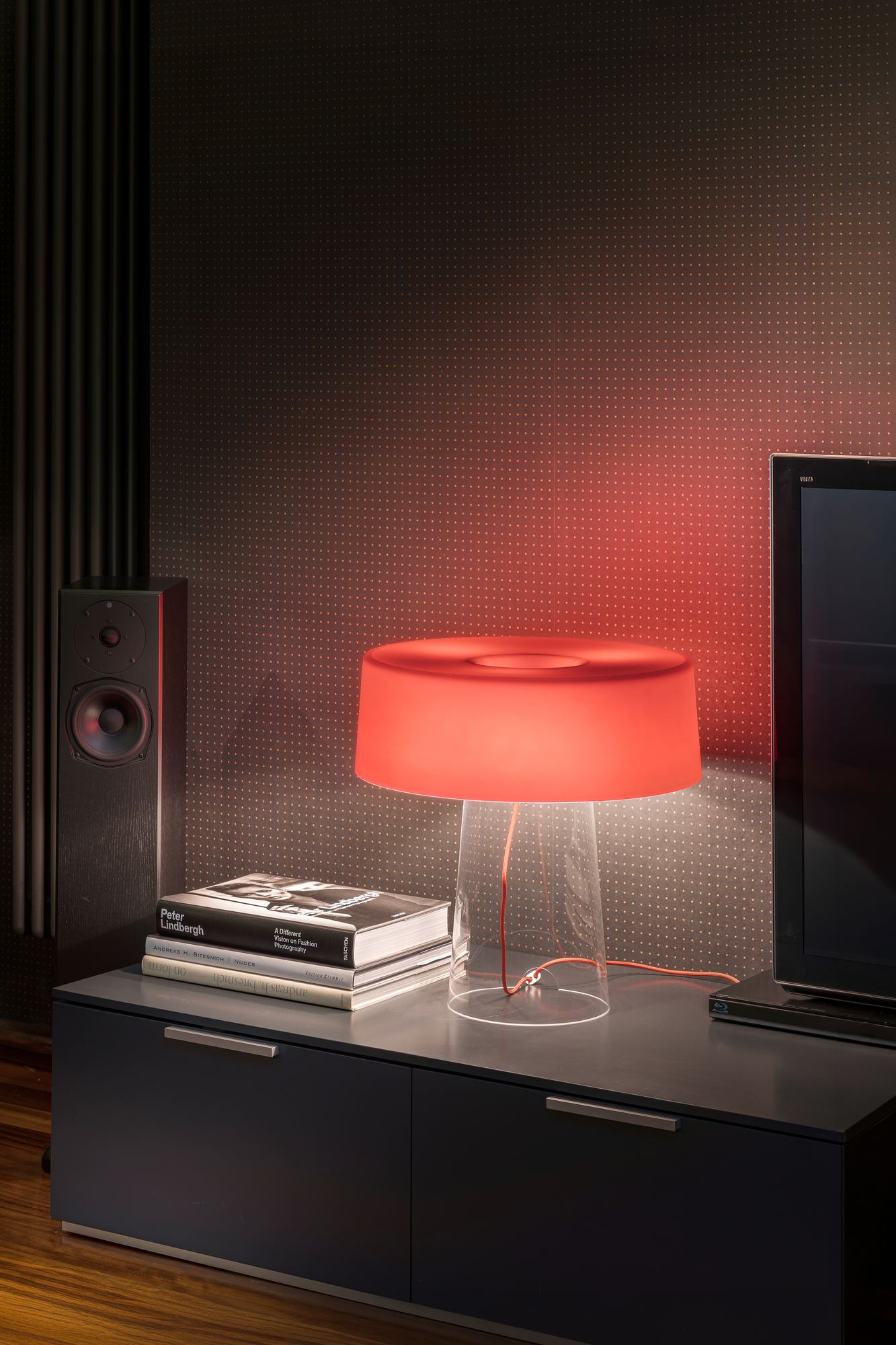 Red glass table lamp on a black cabinet beside the television