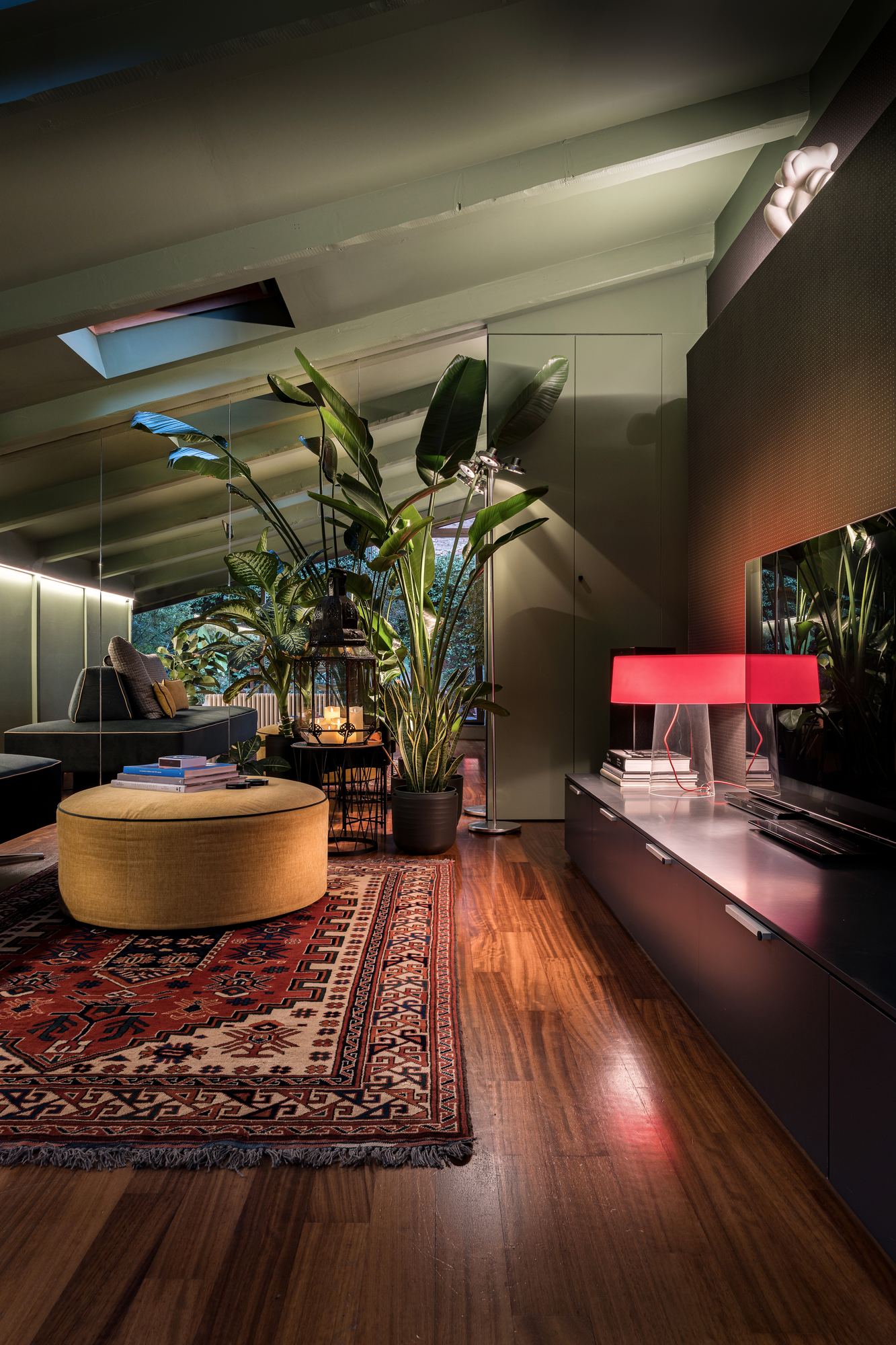 The living room in the evening, with a yellow pouf, plants and the red lamp