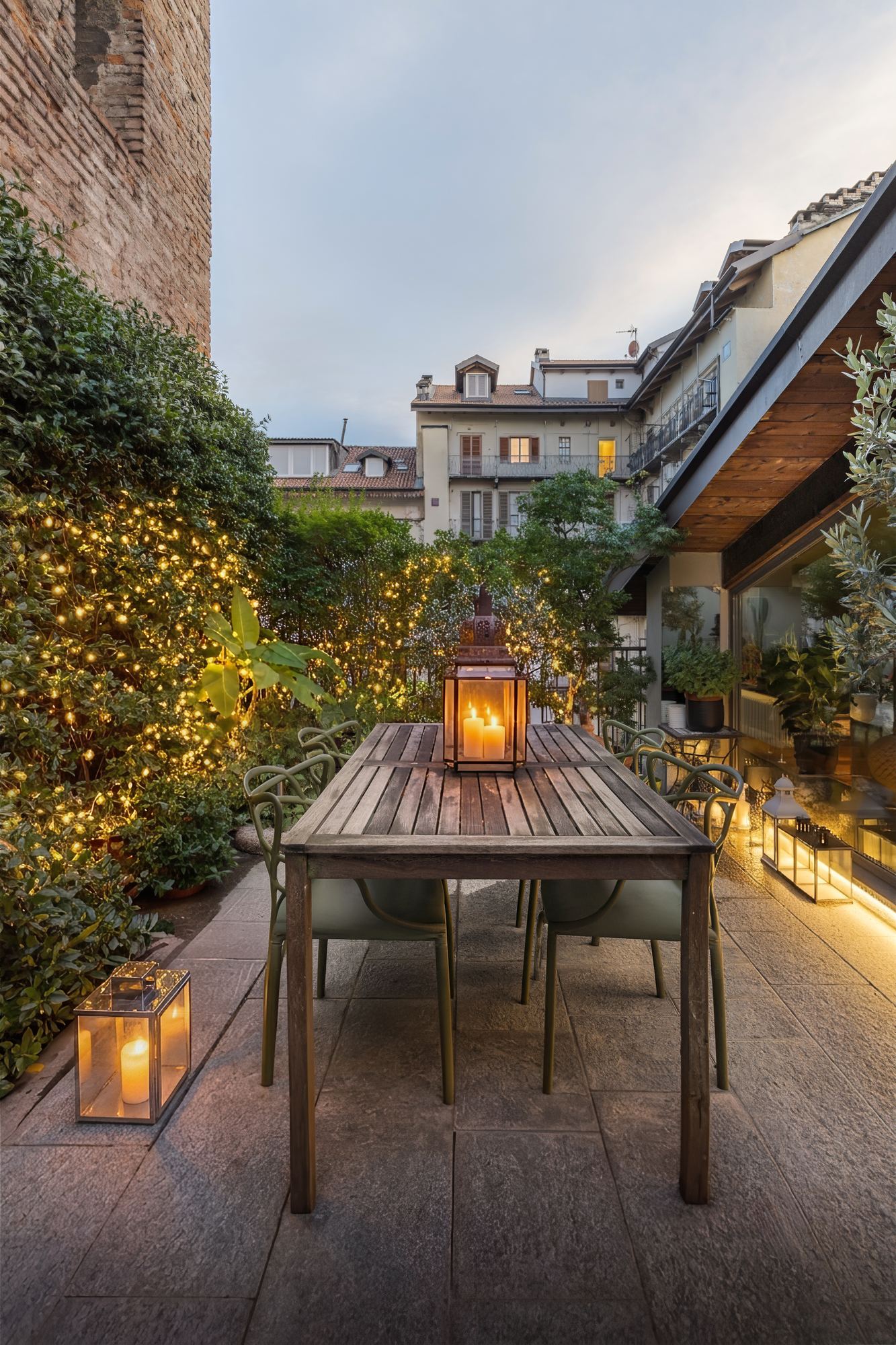 The terrace at dusk: a dining table among plants and lanterns, with rooftops beyond