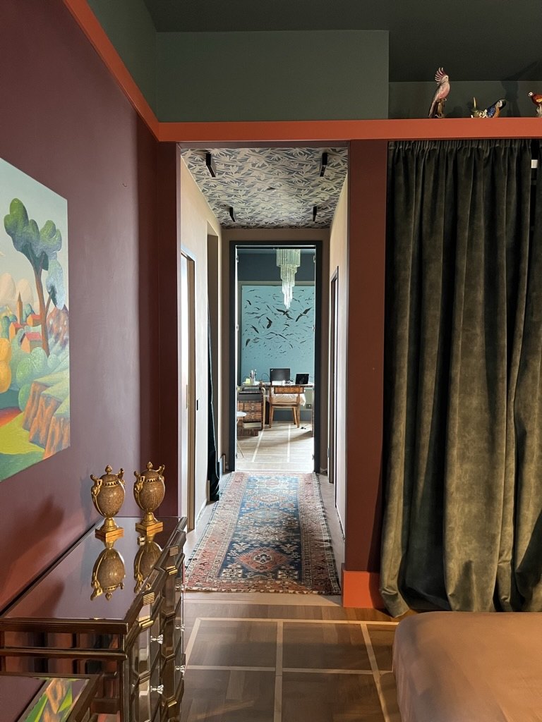 Plum hallway with a mirrored chest, a patterned runner and a green velvet curtain, looking through to a study