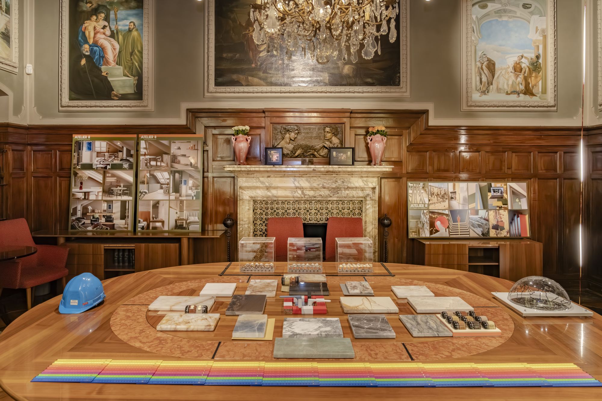 Wood-panelled room with a round table laid with material samples and Atelier 8 boards