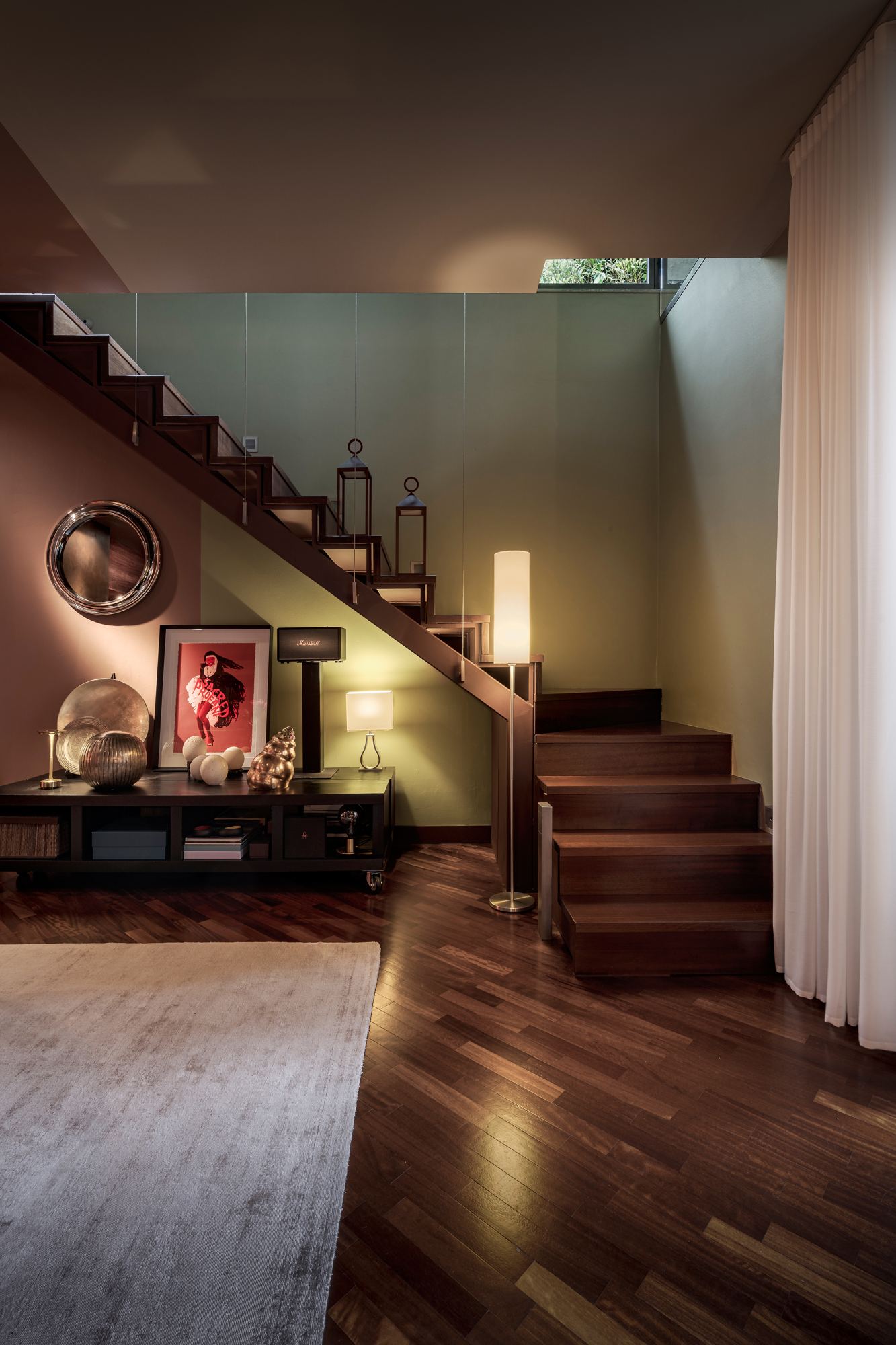 Wooden stair rising from the living room, with a floor lamp and framed art
